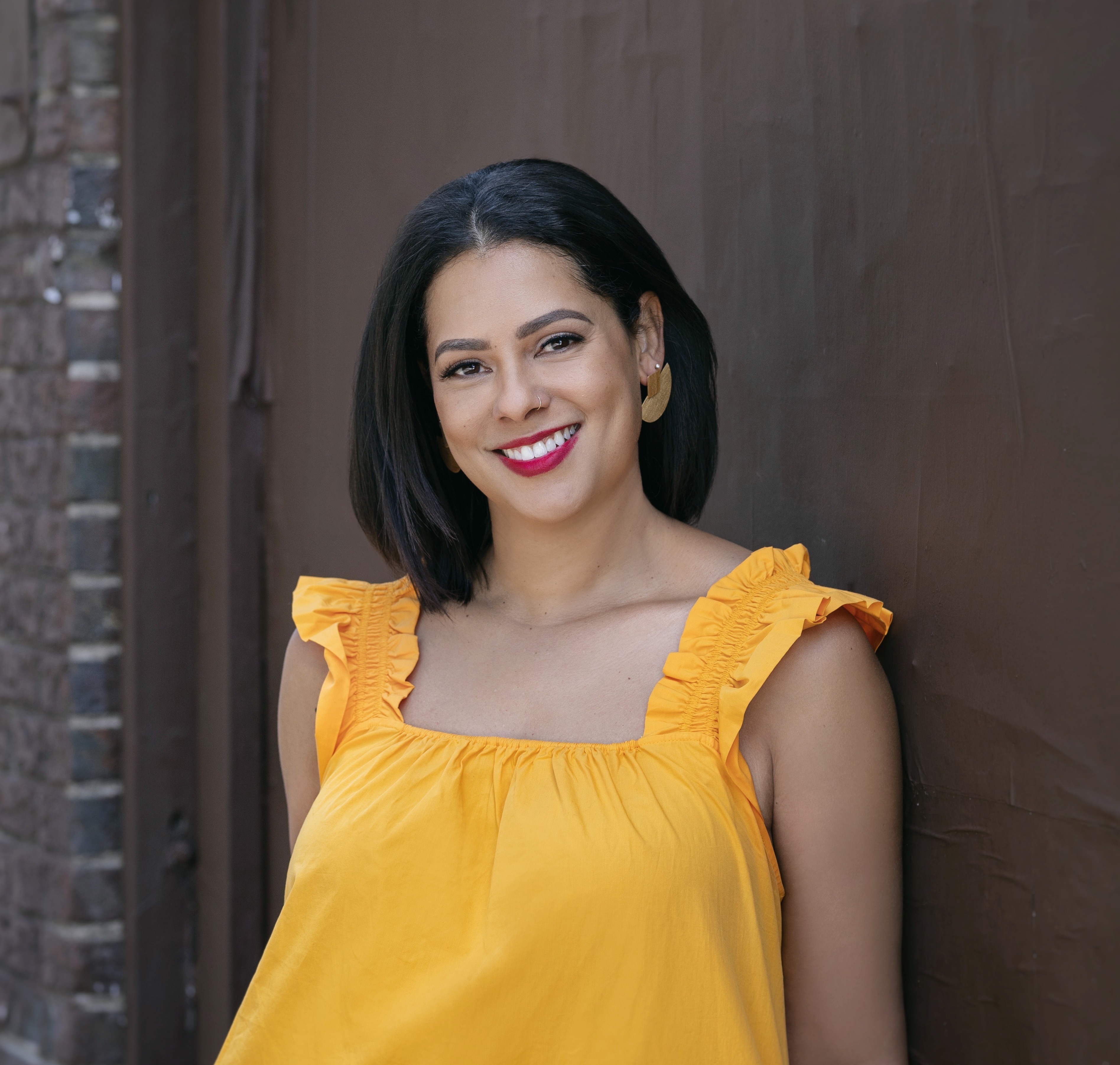 A woman in a yellow dress looks toward the camera and smiles.