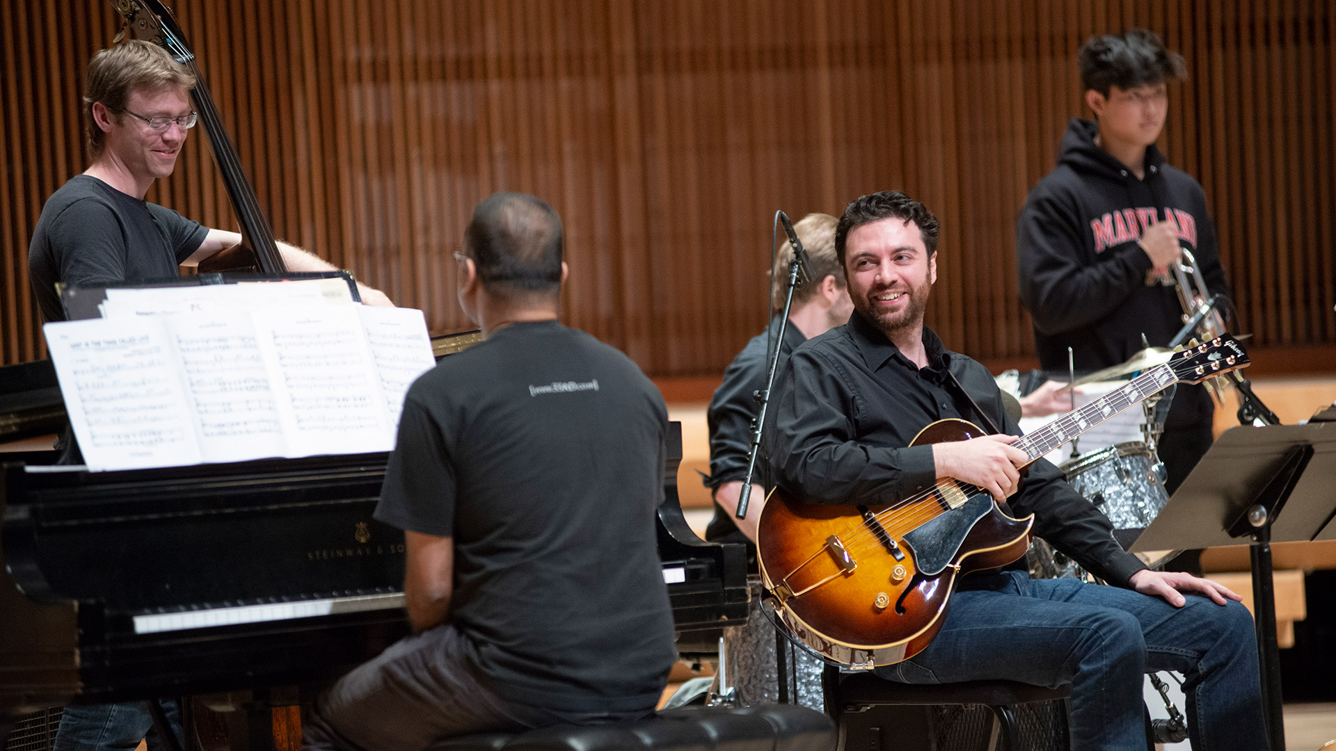  a five person jazz ensemble resting with their instruments. The guitar and double bass players are smiling. 