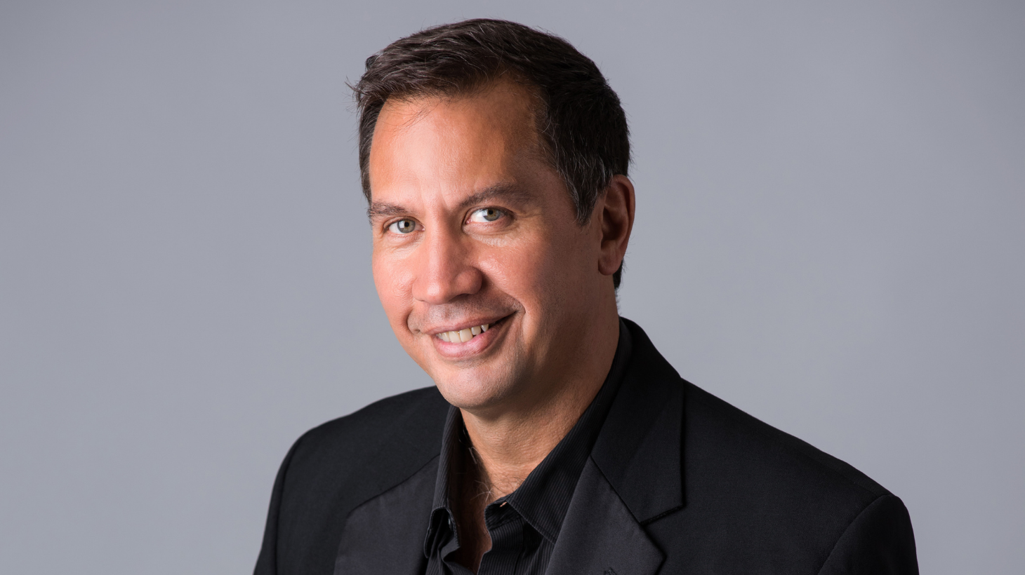 Conductor Daniel Hege in black shirt against gray background