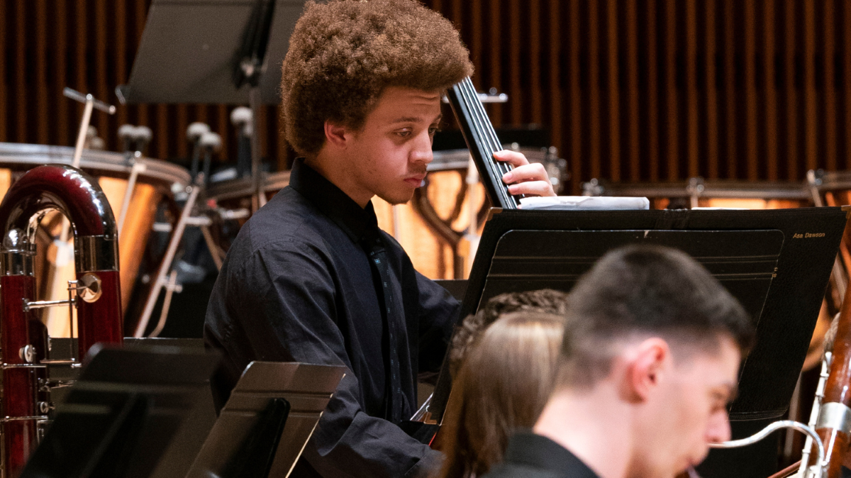 Student reads music and plays cello on stage.