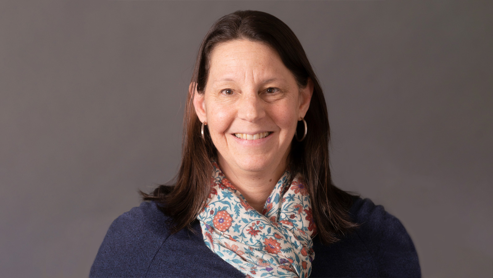 Photo of woman with shoulder-length brown hair against gray background