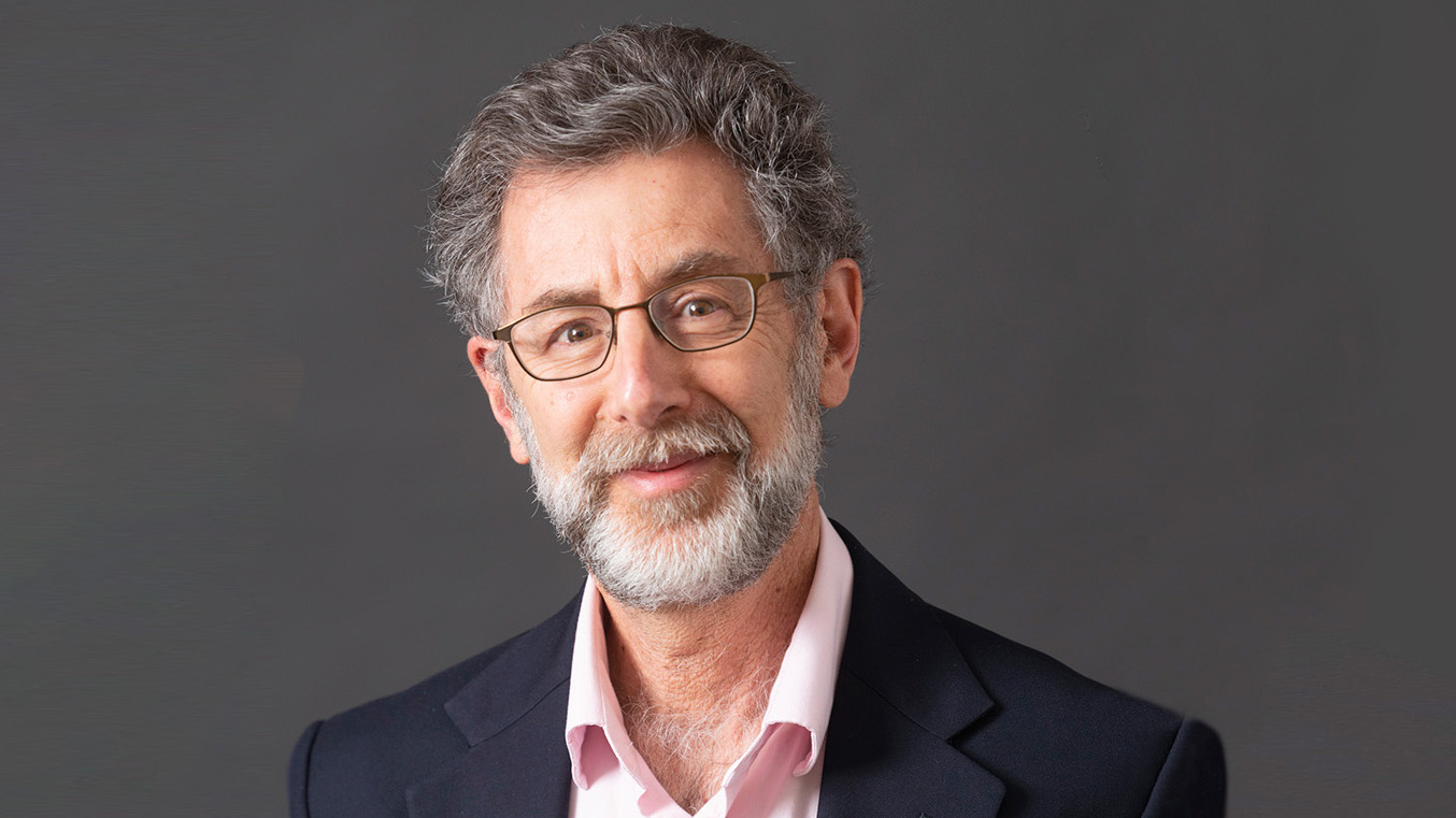 Photo of man with gray hair and beard wearing glasses on gray background