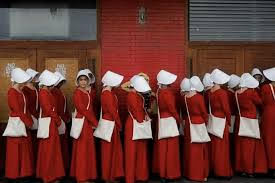 Figures in red dresses and white bonnets in line
