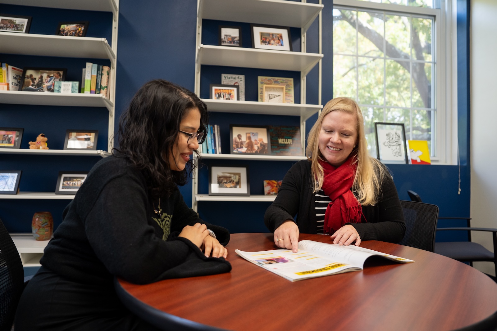 A student and woman sit at a table and look at a brochure together.