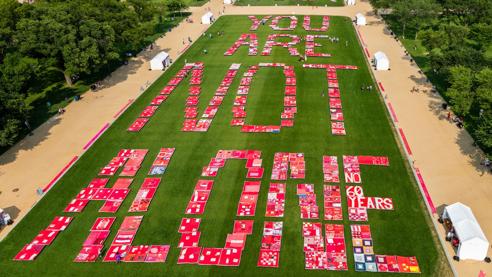 The words "You Are Not Alone" are spelled out on grass using quilts.