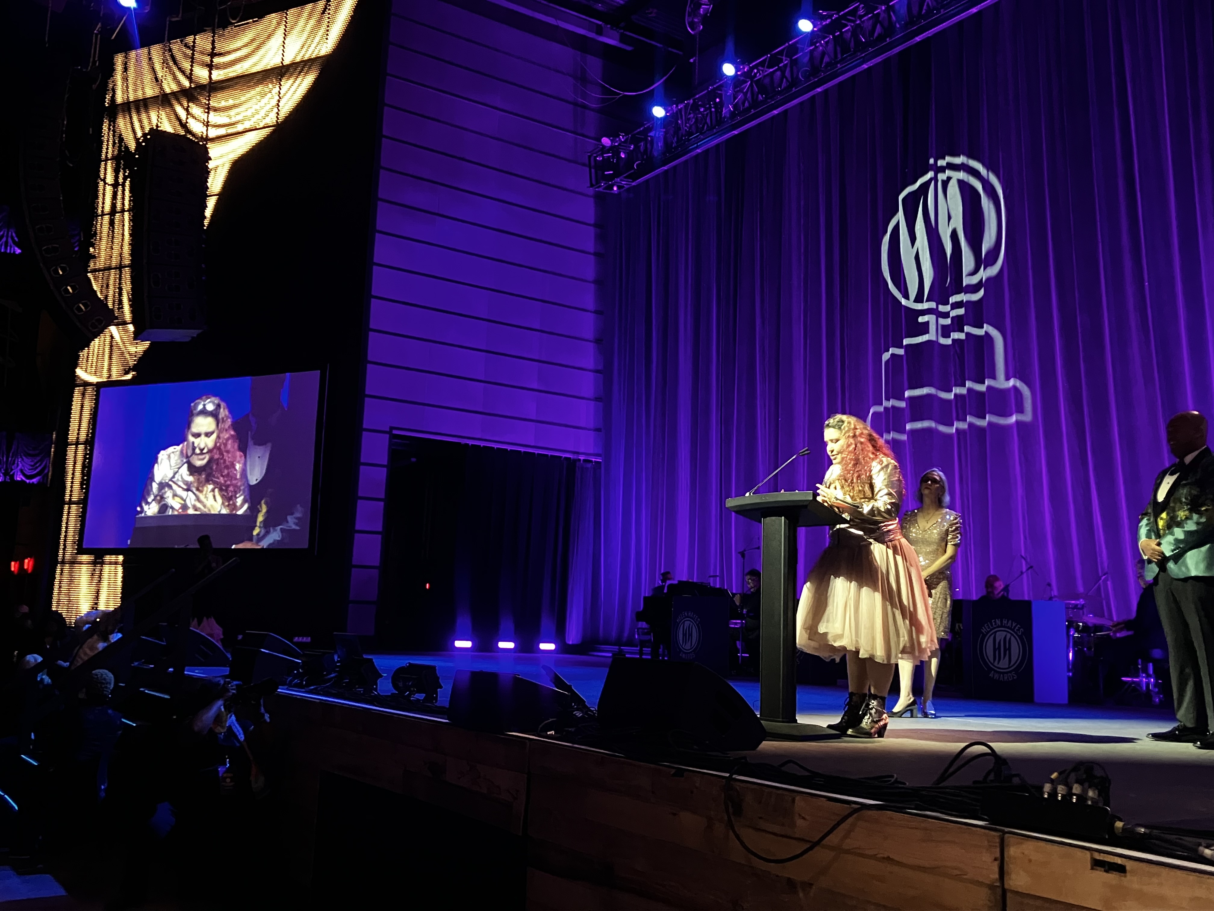 Ivania Stack stands behind a podium on the stage at the Helen Hayes Awards accepting her award.
