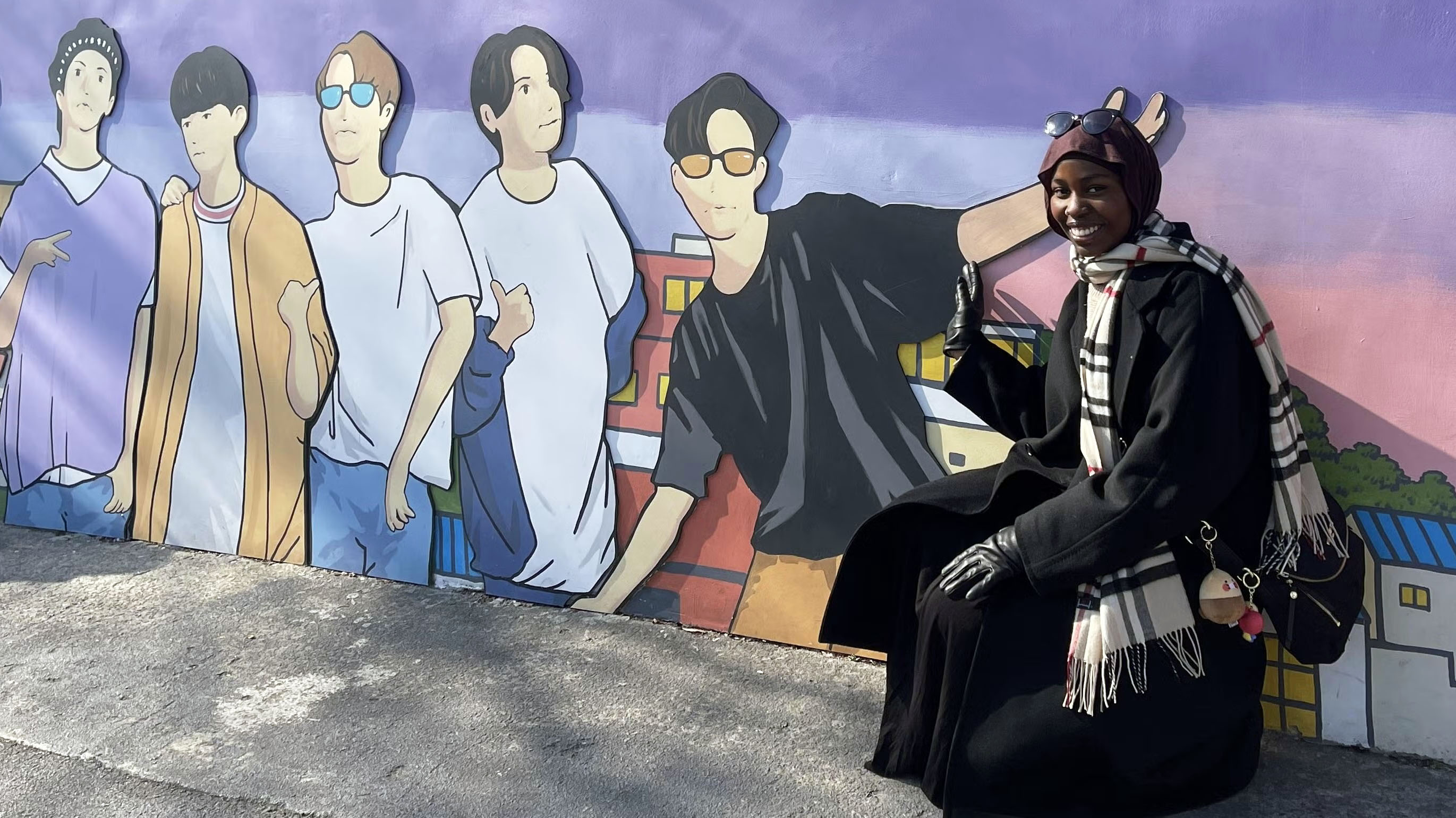 A woman crouches to the right of a mural featuring five men.