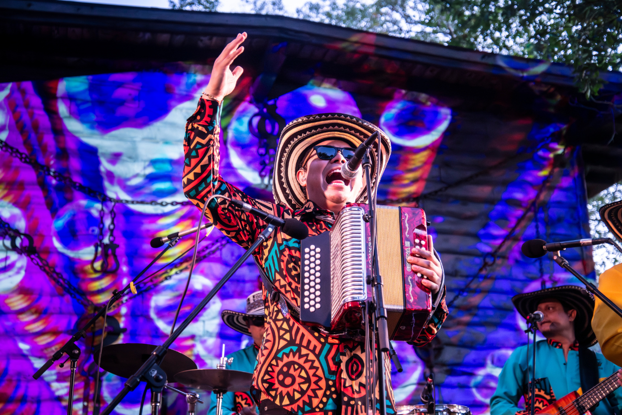 Yeison Landero performs on a vibrant stage, playing an accordion.