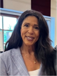 Headshot of an African American woman smiling wearing a gold necklace and a grey and white pinstripe blazer.