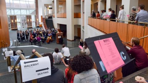 People sit on the stairs in The Clarice's Grand Pavilion to watch a choir perform.