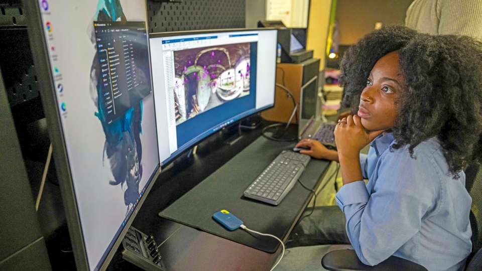 A student sits at a dual-monitor workstation, analyzing a digital project on screen. She leans forward thoughtfully with her chin resting on her hand, highlighting ARHU’s integration of technology and creativity.